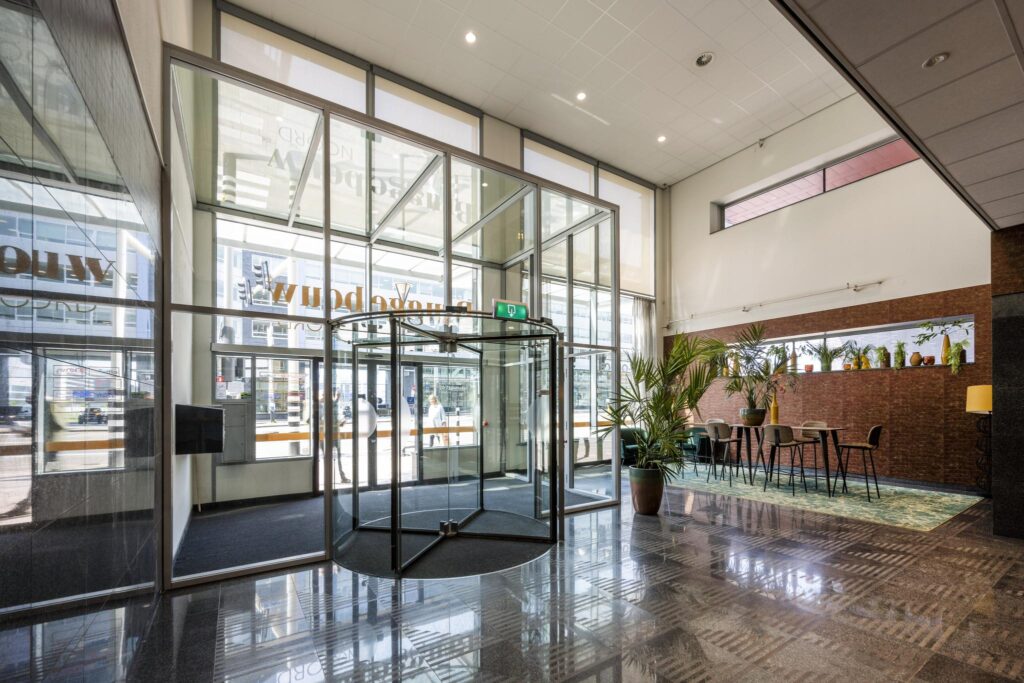 Modern office building entrance at Bos en Lommerplein with a glass revolving door and a stylish seating area.